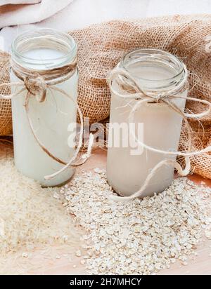 Latte di riso con grani di riso sfuso e latte OAT con avena grezza su una tavola rustica impostazione con spazio copia Foto Stock