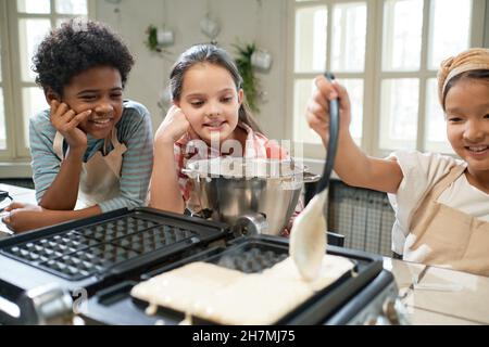 Ragazza che mette l'impasto sull'icona waffle e imparare a cuocere i waffle con i suoi amici in cucina Foto Stock