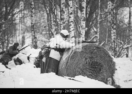 Re-enattore vestito come il soldato tedesco Wehrmacht fanteria nella seconda guerra mondiale mirando Rifle da Hay Roll al giorno d'inverno. Rievocazione storica. Nero e. Foto Stock