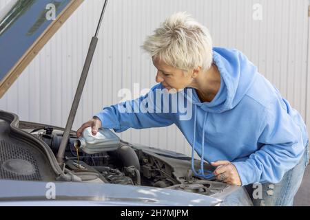 Donna che cambia l'olio nel motore di automobile Foto Stock