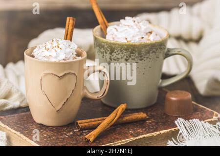 Due tazze di caffè o cioccolata calda con crema e cannella su un vecchio libro su sfondo di legno Foto Stock