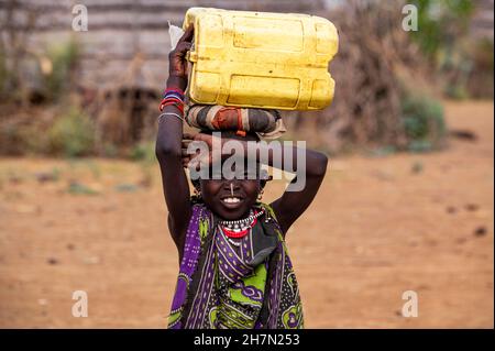 Ragazza vestita tradizionale che porta un contenitore d'acqua, tribù Jiye, Eastern Equatoria state, Sudan del Sud Foto Stock