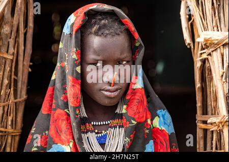 Bambino vestito tradizionale della tribù Jiye seduto nella sua capanna, Eastern Equatoria state, South Sudan Foto Stock