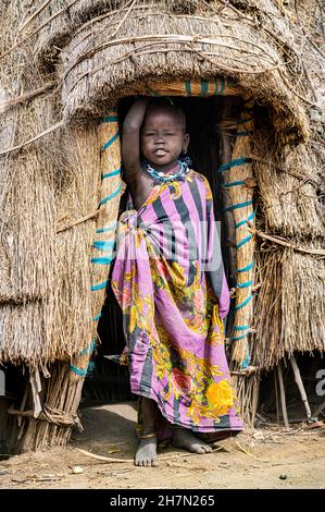 Bambino vestito tradizionale della tribù Jiye in piedi nella sua capanna, Eastern Equatoria state, South Sudan Foto Stock