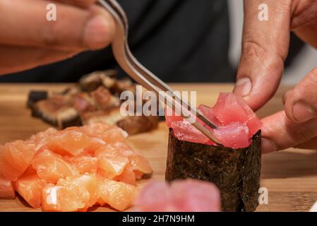 Lo chef prepara gunkan di tonno rosso e alghe nori con le sue pinze metalliche Foto Stock