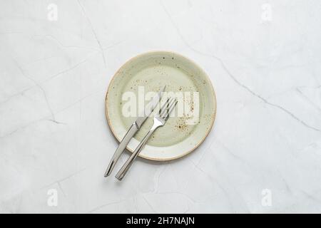 Piatto verde pallido, tocchi grintosi e coltello e forchetta in acciaio inox su tavolo in marmo bianco Foto Stock