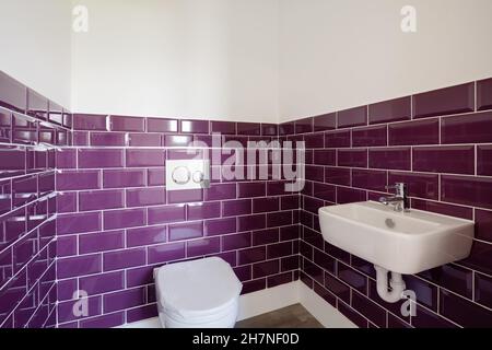 Bagno generico con piastrelle a contrasto viola di colore audace, wc e lavabo Foto Stock