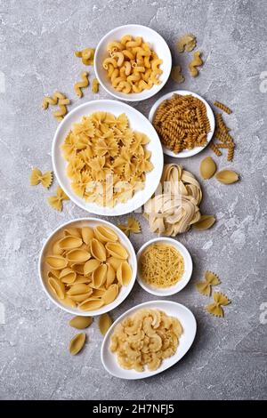 Vista dall'alto sulla varietà di pasta cruda italiana in ciotola bianca su sfondo grigio di cemento Foto Stock