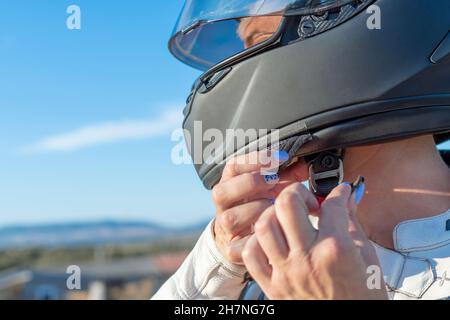 giovane donna biker che fissa il casco di sicurezza per guidare una moto. sicurezza e protezione concetto sulla strada Foto Stock