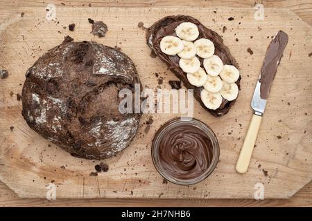 Pane di pasta al cioccolato con crema di nocciole al cioccolato e banana affettata su un asse di legno Foto Stock
