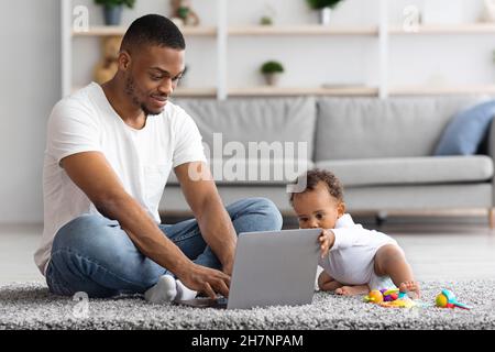 Freelancing con il bambino. Black Man che lavora su un notebook con il bambino Foto Stock