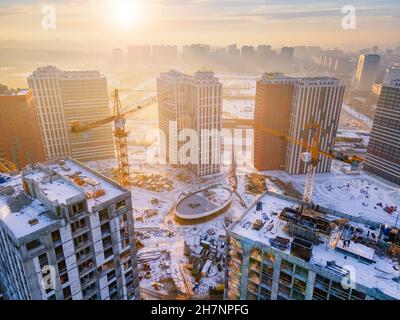 Nuovi quartieri della città al tramonto. Foto aerea del cantiere con gru da costruzione Foto Stock