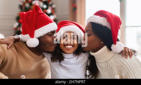 Felice famiglia nera in babbo natale cappelli baciare, festeggiando Natale Foto Stock