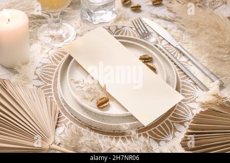 Tavolo posto con carta bianca su tavolo di legno bianco con decorazioni bohémien intorno primo piano. Boho menu di nozze carta mockup. Modello beige tropicale wi Foto Stock