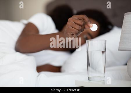 Donna nera che stesa a letto, sciogliendo la medicina in acqua Foto Stock