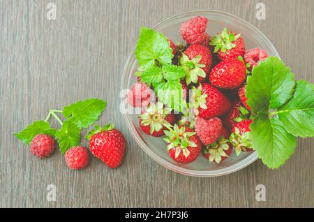 Vista dall'alto di una ciotola di fragole e lamponi con foglie di menta in finitura opaca. Bacche fresche mature. Concetto di cibo sano. Foto Stock