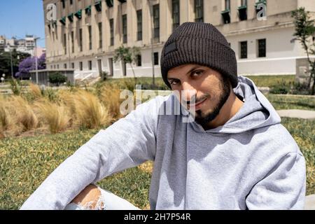 Un giovane uomo latino con un tuta grigia e un berretto in lana nera in stile urbano. Foto Stock