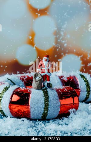 un babbo natale in miniatura che porta un sacco con regali su un falso canne di caramelle e qualche falsa neve che cade su di lui Foto Stock