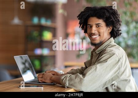 Carriera freelance. Happy Young Black Man che lavora da remoto con il laptop al Cafe Foto Stock