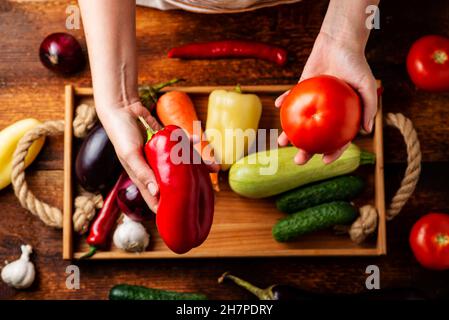 Una donna irriconoscibile sta tenendo un pomodoro su uno sfondo di verdure diverse. Il concetto di cibo sano, vegetarianismo. Foto Stock