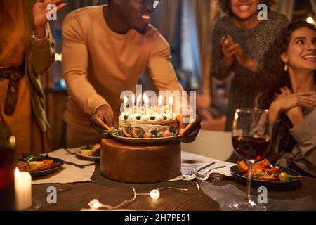 Giovane africano che porta torta di compleanno con candele per il suo amico durante una festa di compleanno Foto Stock