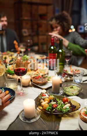 Primo piano del tavolo da pranzo con piatti deliziosi e bicchieri di vino rosso con persone sedute sullo sfondo Foto Stock
