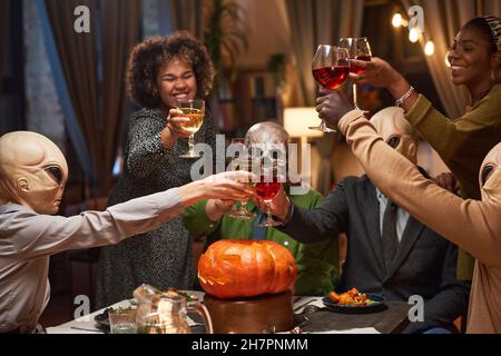 Gruppo di amici felici che tostano con bicchieri di vino rosso e celebrano Halloween durante la festa di casa Foto Stock