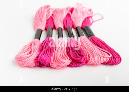 Molti fili da cucito misti rosa vivo per ricami isolati su un tavolo bianco, vista dall'alto o posa piatta di materiali tessili Foto Stock