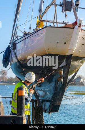 Yacht (Contessa 26) in imbracature da gru a Bosham Quay che vengono lavate a getto per rimuovere l'erbaccia marina e la formazione di incrostazioni al di sotto della linea d'acqua dopo la stagione della vela Foto Stock