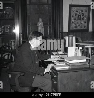 1965, storico, all'interno di una stanza di una chiesa, un giovane ministro maschile della Chiesa di Scozia, seduto alla sua scrivania, inchiostro-penna in mano scrivere note, con vari libri di riferimento a portata di mano, tra cui Dizionario della Bibbia e Libro di preghiera del Ministro, Fife, Scozia, Regno Unito. Foto Stock