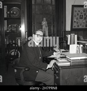 1965, storico, all'interno di una stanza di una chiesa, un giovane ministro maschile della Chiesa di Scozia, seduto alla sua scrivania, inchiostro-penna in mano scrivere note, con vari libri di riferimento a portata di mano, tra cui Dizionario della Bibbia e Libro di preghiera del Ministro, Fife, Scozia, Regno Unito. Foto Stock