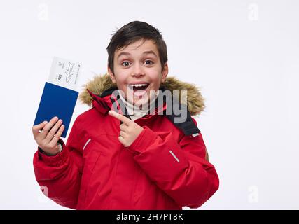 Adorabile ragazzo preadolescente, allegro bambino di scuola in rosso luminoso caldo parka punti con il dito a un passaporto con un biglietto e carta d'imbarco, isola Foto Stock