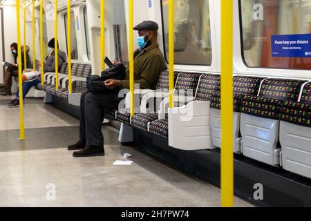 Uomo più anziano seduto da solo in tubo TFL carro sotterraneo che indossa un facemask covid con posti vuoti nel novembre 2021 Londra Inghilterra Regno Unito KATHY DEWITT Foto Stock