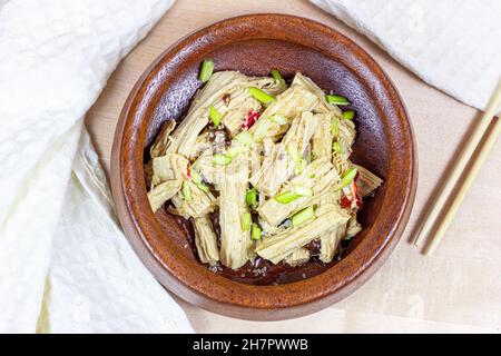 Vista dall'alto dell'insalata fushu asiatica (bastoncini yuba, curd di soia, pelle di tofu) in un recipiente di legno rotondo su sfondo chiaro. Foto Stock