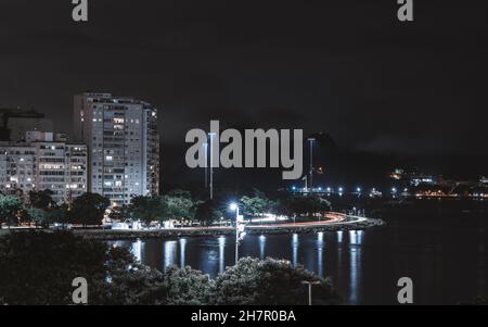 Un paesaggio urbano notturno bluastro a lunga esposizione con una baia sulla destra e un gruppo di edifici residenziali con una svolta a sinistra, Botafogo distr Foto Stock