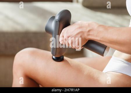 Auto-massaggio delle gambe delle donne con una pistola perfezionante a casa. Massaggio antiurto per ripristinare i muscoli della plancia e i punti di attivazione Foto Stock