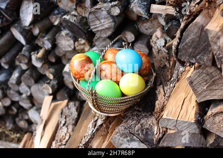 Uova di Pasqua colorate e brillanti in un cestino sul mucchio di legna all'aperto Foto Stock