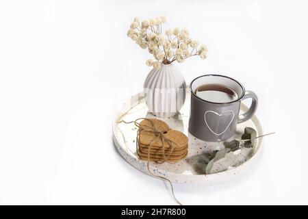 Un vaso con fiori bianchi secchi, una tazza di smalto grigio con un cuore disegnato con il tè, con biscotti di pan di zenzero stand su un vassoio per San Valentino. Spazio di copia Foto Stock