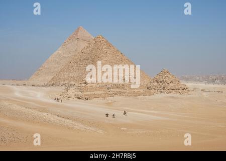 Vista su Khafre, Menkaure e piramidi delle Regine dal deserto. Numerosi cavalieri di cavalli e cammelli nel telaio. Foto Stock