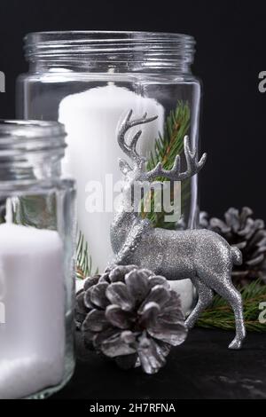 Cervi di Natale in argento sullo sfondo di candele e coni su sfondo nero. Primo piano. Foto Stock