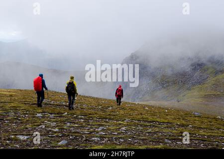 Scottish Highlands, Regno Unito - 7 agosto 2017: Tre escursionisti che si dirama in abbigliamento e zaini all'aperto in condizioni climatiche avverse attraversando un altopiano di montagna Foto Stock