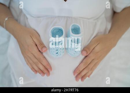 Taglia la donna irriconoscibile che giace con le scarpe del bambino sul pancino Foto Stock