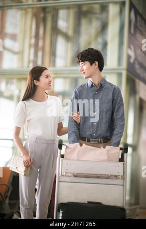 Giovane coppia che spinge i bagagli all'aeroporto Foto Stock