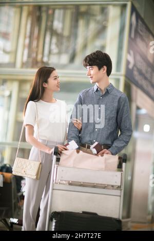 Giovane coppia che spinge i bagagli all'aeroporto Foto Stock