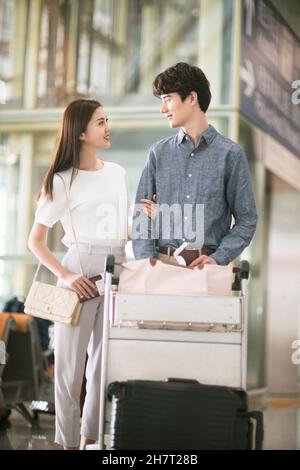 Giovane coppia che spinge i bagagli all'aeroporto Foto Stock