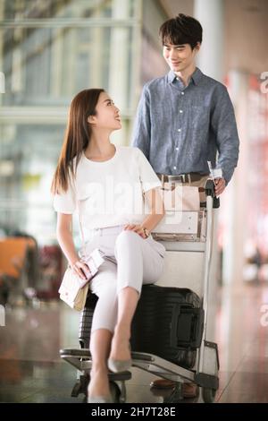 Giovane coppia che spinge i bagagli all'aeroporto Foto Stock