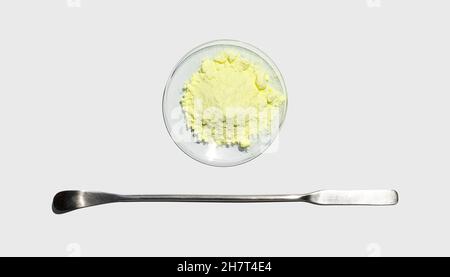 Polvere di zolfo in vetro da orologio chimico posta accanto alla spatola in acciaio inox sul tavolo da laboratorio. Foto Stock