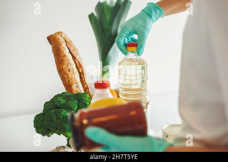 Le mani della donna che mettono i generi alimentari fuori dalla scatola di donazione su sfondo bianco. Quarantena di servizio coronavirus pandemico. Mani che preparano la scatola di donnation Foto Stock