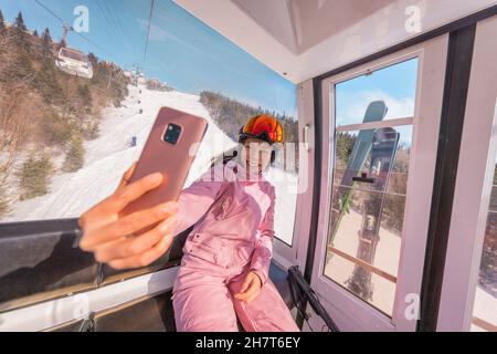 Vacanza sci - sciatore donna in sciovia gondola facendo selfie foto o video con il telefono. Concetto di vacanze invernali sugli sci. Sciare sulle piste da neve in Foto Stock