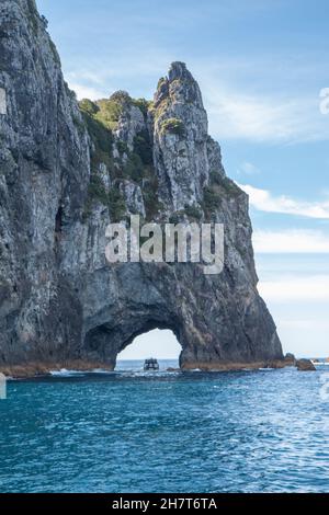 Una singola barca che passa attraverso il Hole in the Rock a Piercy Island, Capo Brett, Bay of Islands Foto Stock